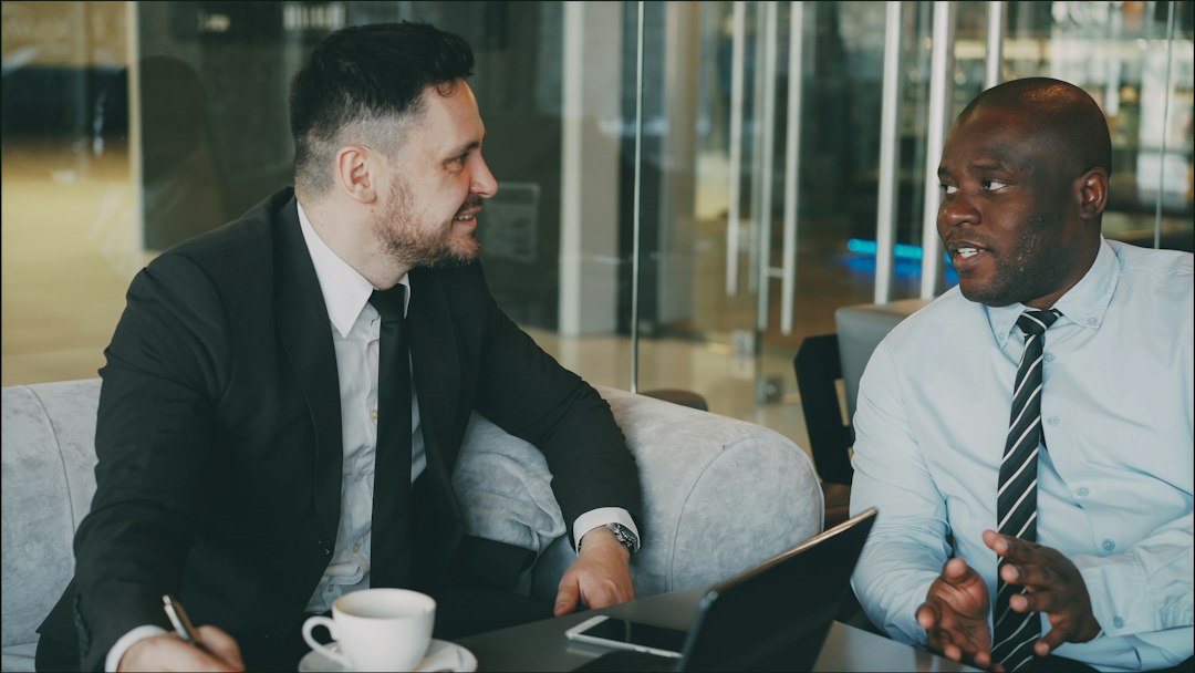 A professional real estate agent sits at a clean, modern desk, calmly explaining documents to a young couple in a bright, welcoming office.